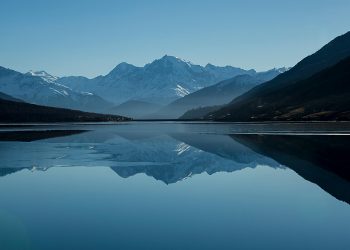 Snow-capped mountains reflected in a calm alpine lake Mountain lake reflecting snow-capped peaks under blue sky